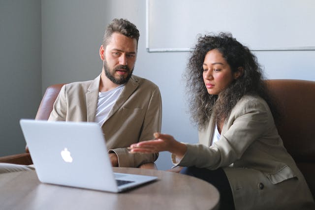 a man and a woman discussing something infront of a laptop